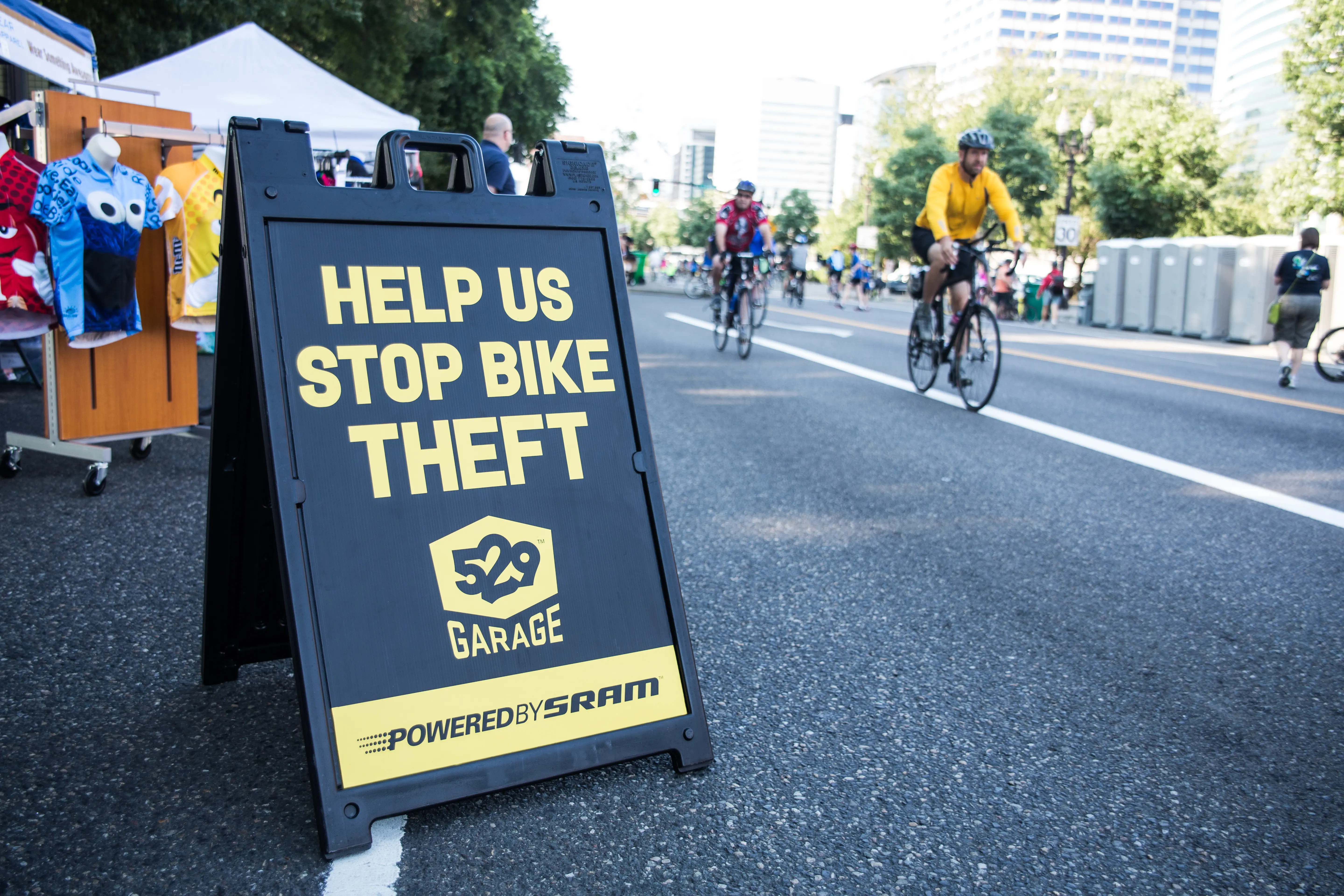 Black-and-white photo of dozens of bicycles neatly racked in rows, viewed from behind the seats. Each bike displays a race number, and some have water bottles attached.